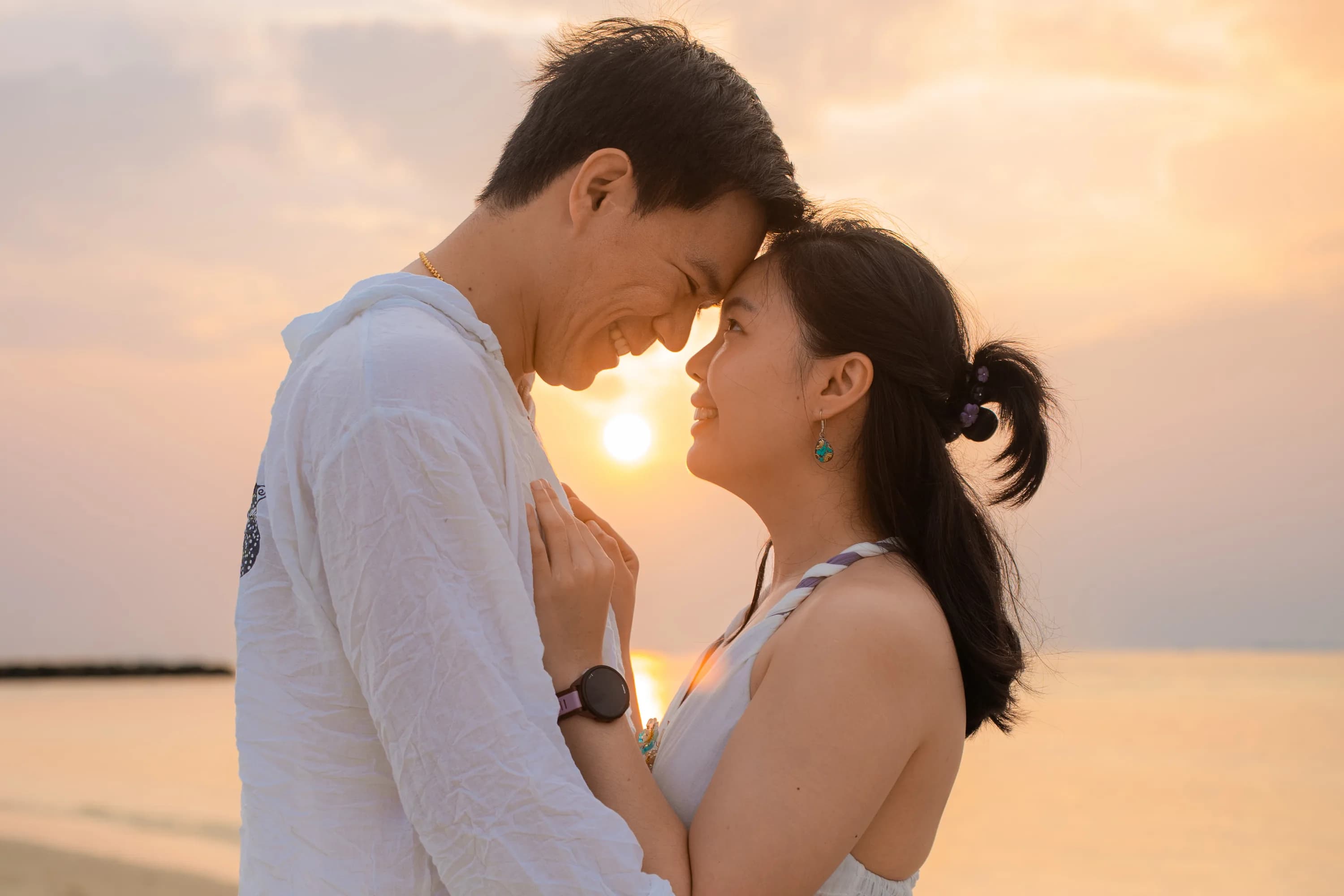 Couple at golden hour on a Maldives beach with turquoise water behind them, photographed by Coora Studio